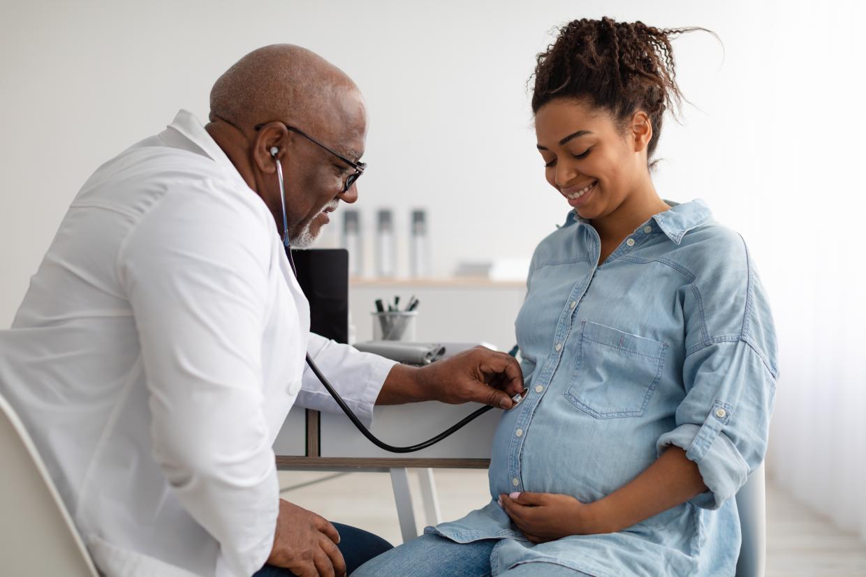 Male doctor listening to a pregnant woman's belly with a stethoscope